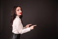 Portrait of smiling young businesswoman pointing finger away over black background and looking at camera. Copy space Royalty Free Stock Photo