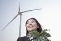 Portrait of smiling young businesswoman standing by a wind turbine and holding a plant Royalty Free Stock Photo