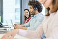 Portrait of smiling young businesswoman using headset and laptop with colleagues in foreground at office Royalty Free Stock Photo