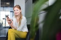 Portrait of smiling young businesswoman using mobile phone on chair in office Royalty Free Stock Photo