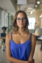 Portrait Of Smiling Young Businesswoman Wearing Glasses Standing In Busy Office Royalty Free Stock Photo