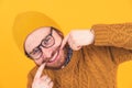 Portrait of smiling young Caucasian man in glasses, hat and beard, man touching his edges of mouth, showing teeth orange Royalty Free Stock Photo