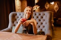 Portrait of young charming woman in evening dress, sitting on sofa in restaurant with glass of alcohol in her hands. Royalty Free Stock Photo