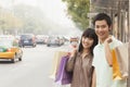 Portrait of smiling young couple carrying colorful shopping bags and waiting for the bus at the bus stop, Beijing, China Royalty Free Stock Photo