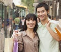 Portrait of smiling young couple carrying colorful shopping bags and waiting for the bus at the bus stop, Beijing, China Royalty Free Stock Photo