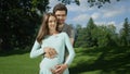 PORTRAIT: Embraced pregnant couple standing in a green meadow on a sunny day Royalty Free Stock Photo