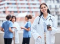 Portrait of smiling young doctor enjoying a cup of coffee outside with her colleagues in the background. Happy medical Royalty Free Stock Photo