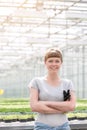 Portrait of smiling young female botanist standing with arms crossed against herbs in greenhouse