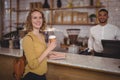 Portrait of smiling young female customer holding disposable coffee cup at counter against waiter Royalty Free Stock Photo