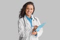 Portrait of smiling young female doctor in uniform holding clipboard, looking and smiling at camera, grey background Royalty Free Stock Photo