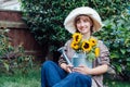 Portrait of smiling young female farmer woman holding watering can with fresh sunflowes bouquet while sitting in the Royalty Free Stock Photo