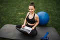 Portrait of a smiling young fitness girl using laptop computer while sitting on a mat outdoors Royalty Free Stock Photo