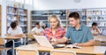 Portrait of smiling young girl and boy looking at laptop screen while studying with group of students in library Royalty Free Stock Photo