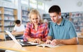 Portrait of smiling young girl and boy looking at laptop screen while studying with group of students in library Royalty Free Stock Photo