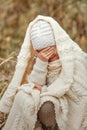 Portrait of a smiling young girl sitting in a park wrapped in a white blanket