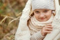 Portrait of a smiling young girl sitting in a park wrapped in a white blanket