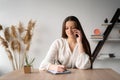 portrait of a smiling young girl sitting at the table talking on the phone and making notes in a work notebook while Royalty Free Stock Photo