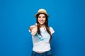 Portrait of a smiling young girl wearing beach hat and showing thumbs up gesture isolated over blue Royalty Free Stock Photo