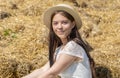 Portrait of a smiling young girl of 17-20 years old in a straw hat and a white dress against the background of bales of dried stra
