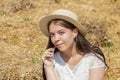 Portrait of a smiling young girl of 17-20 years old in a straw hat and a white dress against the background of bales of dried stra