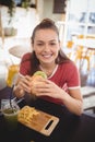 Portrait of smiling young gorgeous woman eating burger at coffee shop Royalty Free Stock Photo