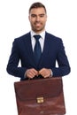 portrait of smiling young guy in navy blue suit proudly holding suitcase