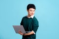 Portrait of a smiling young handsome Asian man holding laptop computerand looking sideways in isolated studio blue background Royalty Free Stock Photo