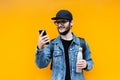 Portrait of smiling young hipster guy, holding steel thermo eco bottle for water and looking in smartphone, on orange background. Royalty Free Stock Photo