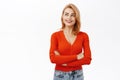 Portrait of smiling young hopeful girl looking aside, holding hands crossed on chest, standing over white background