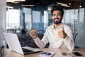 Portrait of a smiling young Indian man sitting in the office at the desk, holding a credit card in his hand and showing Royalty Free Stock Photo