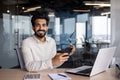 Portrait of a smiling young Indian man sitting in the office at the desk, holding glasses and a mobile phone, looking Royalty Free Stock Photo