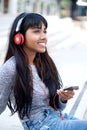 Smiling young Indian woman sitting outside with mobile phone and headphones Royalty Free Stock Photo