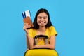 Portrait of smiling young korean lady with down syndrome in yellow t-shirt with suitcase show passport, air ticket Royalty Free Stock Photo