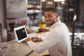 Portrait of smiling young male owner sitting with laptop at counter Royalty Free Stock Photo