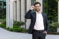 Portrait of a smiling young man in a business suit standing near an office building, holding glasses and smiling at the Royalty Free Stock Photo