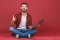 Portrait of a smiling young man in casual holding laptop computer while sitting on a floor and showing thumbs up gesture isolated Royalty Free Stock Photo