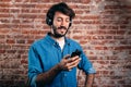 Portrait of smiling young man with earphones and cell phone. Casual wear and brick wall of background Royalty Free Stock Photo