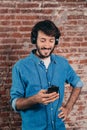 Portrait of smiling young man with headphones and cell phone. Casual wear and brick wall of background Royalty Free Stock Photo