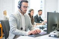 Portrait of a smiling young man with headset using computer in the office. Royalty Free Stock Photo