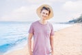 Portrait of smiling young man in a pink t shirt and straw female hat and sunglasses on his head standing on a sea beach Royalty Free Stock Photo