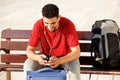 Smiling young man sitting with bags and looking at mobile phone Royalty Free Stock Photo