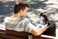Smiling young man sitting on bench outdoors with bag and using smart phone Royalty Free Stock Photo