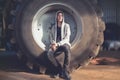 Smiling young man sitting in a huge wheel of a tractor Royalty Free Stock Photo