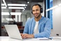 Portrait of a smiling young man sitting in the office with a laptop in headphones and looking confidently into the Royalty Free Stock Photo