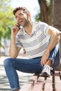 Smiling young man sitting outdoors on bench and talking on mobile phone Royalty Free Stock Photo