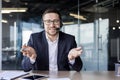 Portrait of a smiling young man in a suit and headset sitting in the office at the desk and talking to the camera Royalty Free Stock Photo