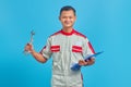 Portrait of a smiling young mechanic holding clipboard and showing wrench isolated on blue background Royalty Free Stock Photo