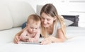 Portrait of smiling young mother baby boy lying on bed and using digital tablet Royalty Free Stock Photo