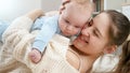 Portrait of smiling young mother hugging and embracing her little baby son while lying on floor. Concept of family Royalty Free Stock Photo