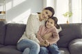 Portrait of a smiling young mother hugging her little daughter sitting on sofa at home. Royalty Free Stock Photo